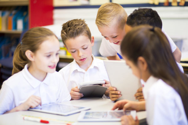 Friends in the Classroom Happy students in classroom using a digital tablet, they are all wearing uniforms.