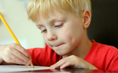Young Child Drawing on Paper with Pencil a young, preschool aged child is drawing on a white piece of paper with a writing pencil